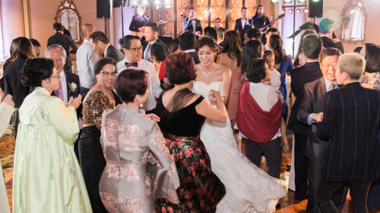 A lively wedding reception scene at the Langham Huntington, Pasadena featuring a diverse group of guests dancing joyfully while a talented 20-piece wedding band performs in the background. The image captures the vibrant atmosphere created by Ben Mallare Events & Entertainment, showcasing the excitement and energy that live wedding bands bring to special occasions. Guests of all ages enjoy the music and celebrate together, highlighting the importance of live entertainment in creating unforgettable wedding memories.